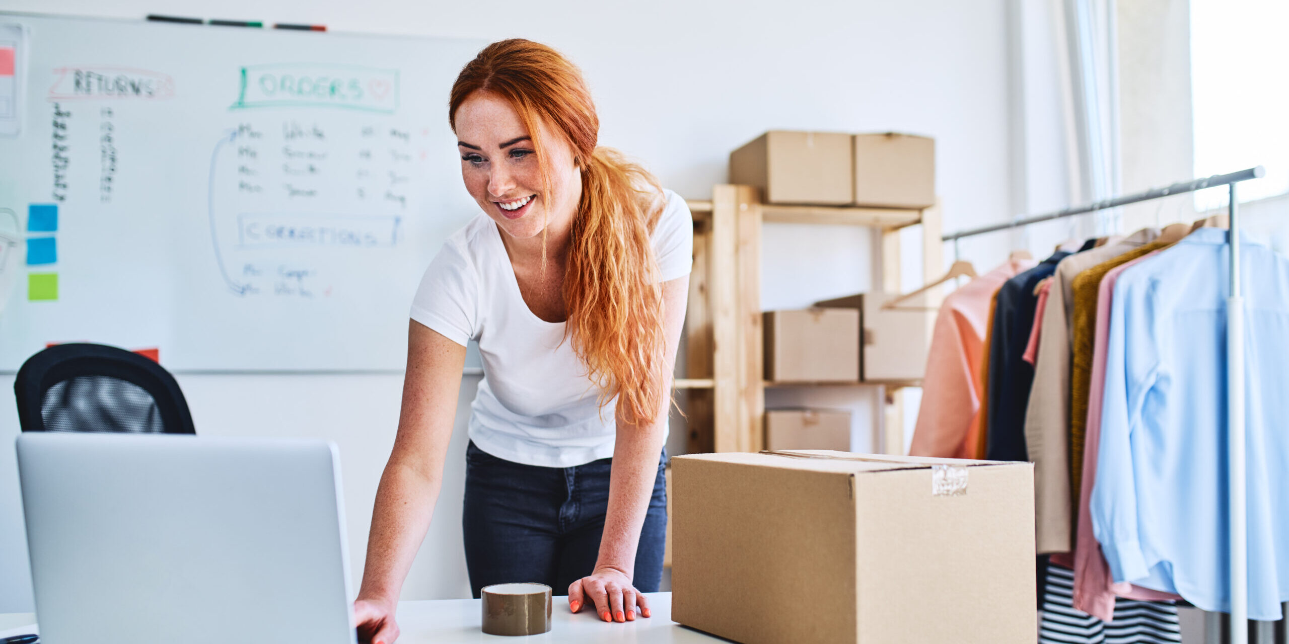 Young business owner looking at laptop while preparing eCommerce deliveries.