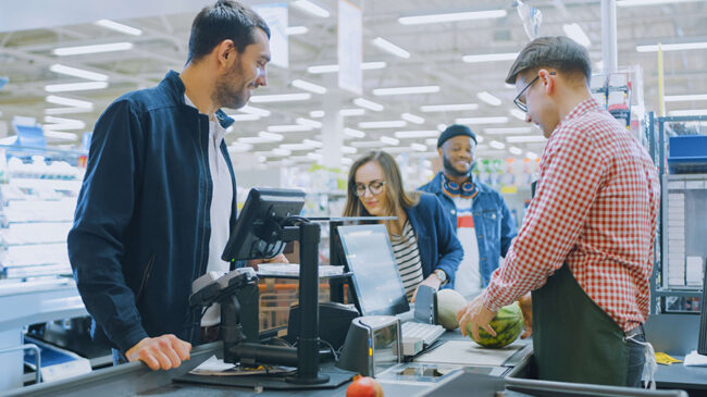 At the Supermarket: Checkout Counter Professional Cashier Scans Groceries and Food Items. Clean Modern Shopping Mall.